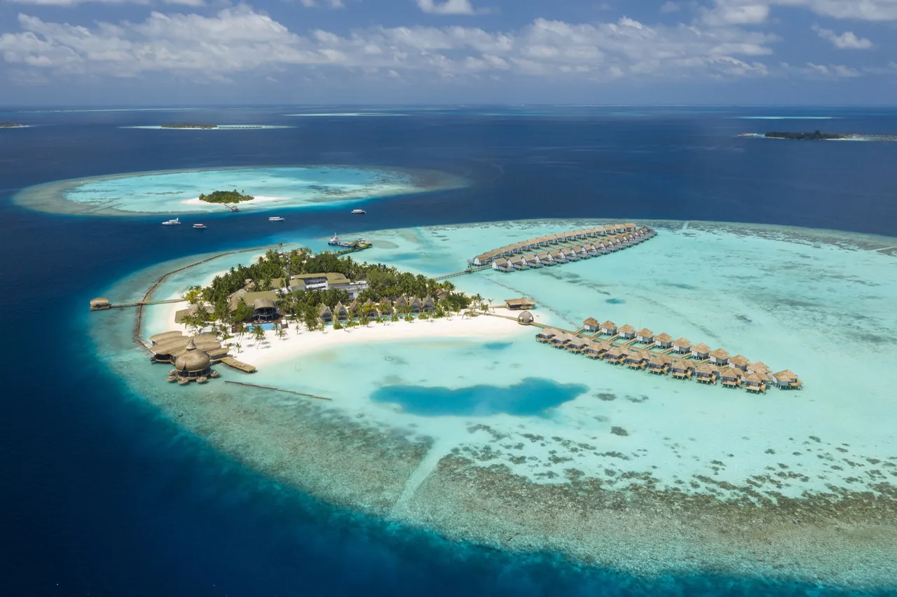Aerial view of Maafushivaru atoll with a resort island, water villas and reef